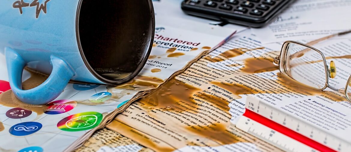 Ausgelaufene Kaffetasse auf Papieren im Büro